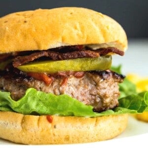 A cooked duck burger in a bun topped with pickles, lettuce and tomato.