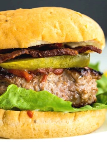 A cooked duck burger in a bun topped with pickles, lettuce and tomato.