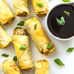 A plate of cooked egg rolls with a side of soy sauce.