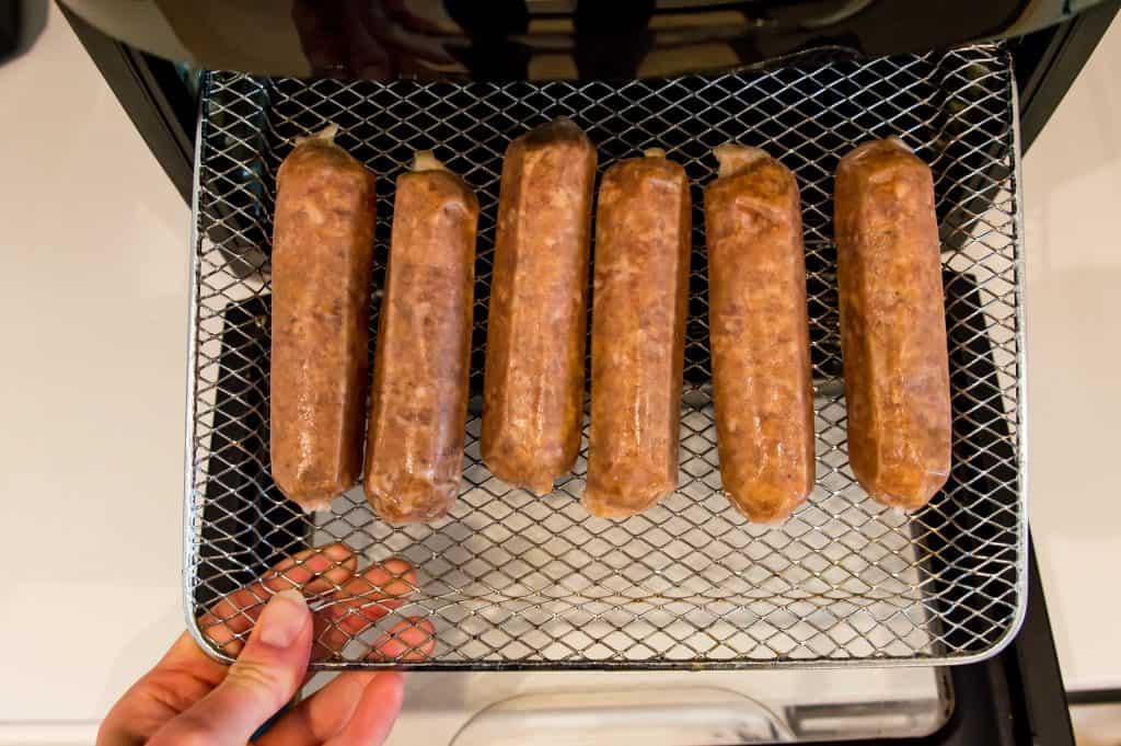 Six bratwurst sausages on an air fryer tray.