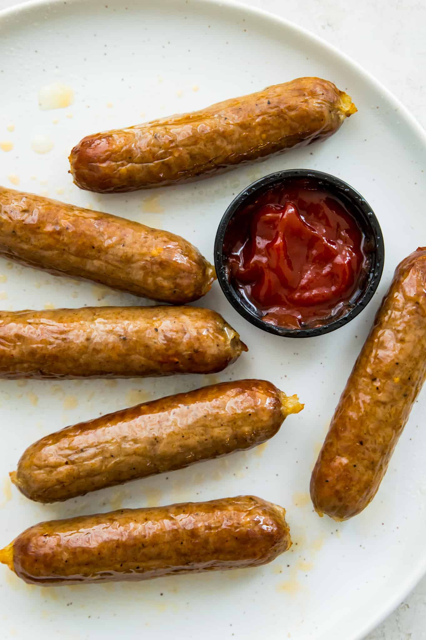 A plate with cooked brats with a dish full of ketchup beside them.