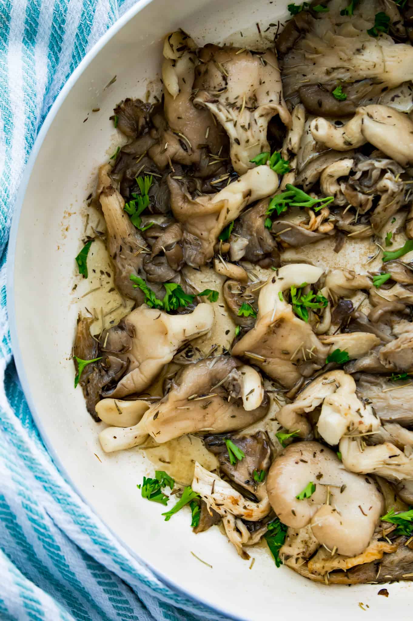 A pan of cooked oyster mushrooms with fresh herbs on top.