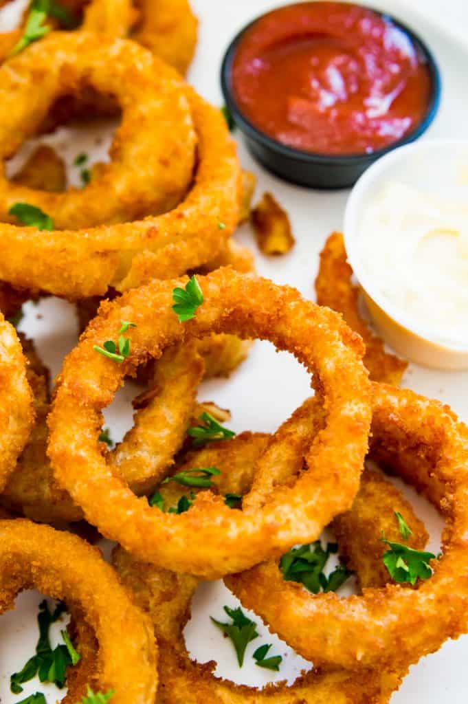 A plate full of cooked onion rings with a side of ketchup