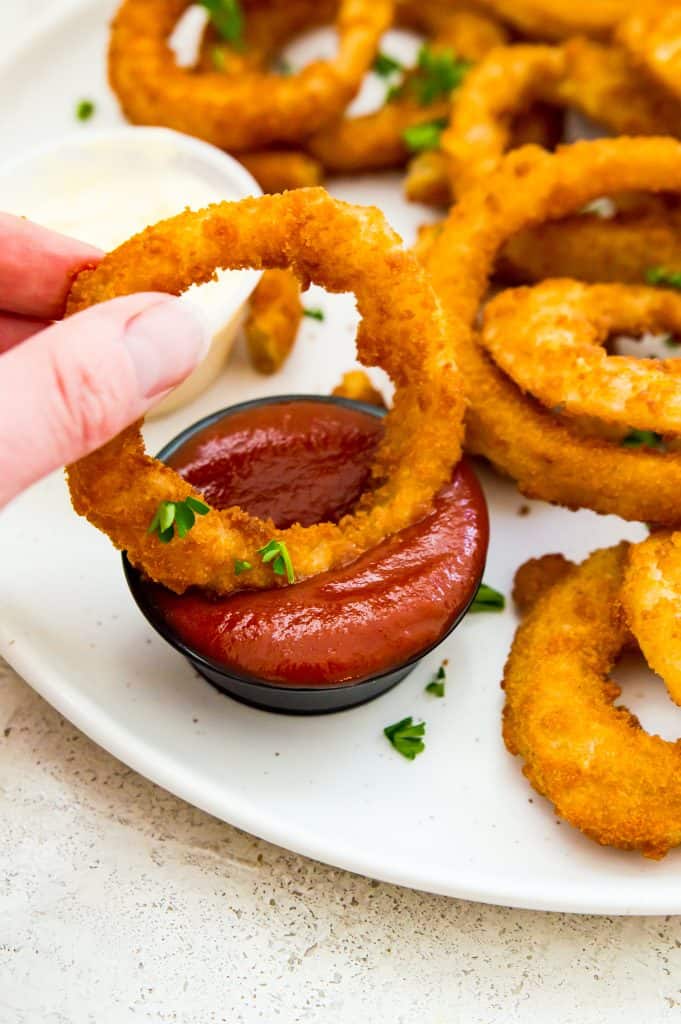 A cooked onion ring being dipped in a bowl of of ketchup