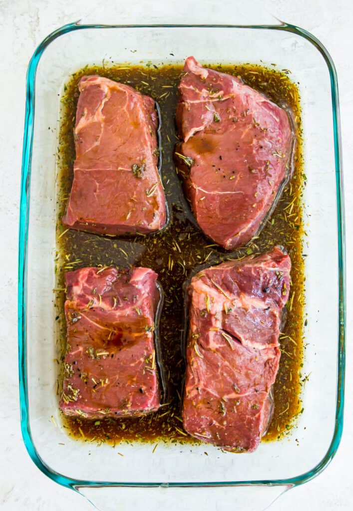 Four steaks marinading in a glass baking dish.