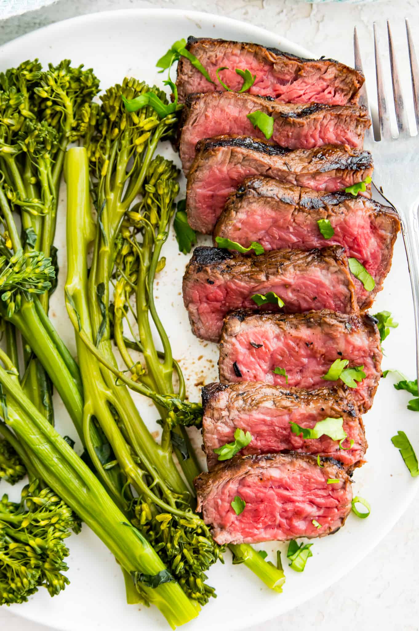 A plate of cut, cooked steak with cooked broccoli beside it.