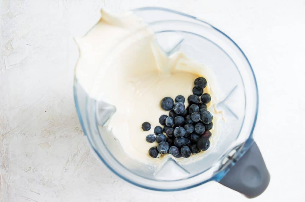 Fresh blueberries and vegan cheesecake ingredients in a blender.