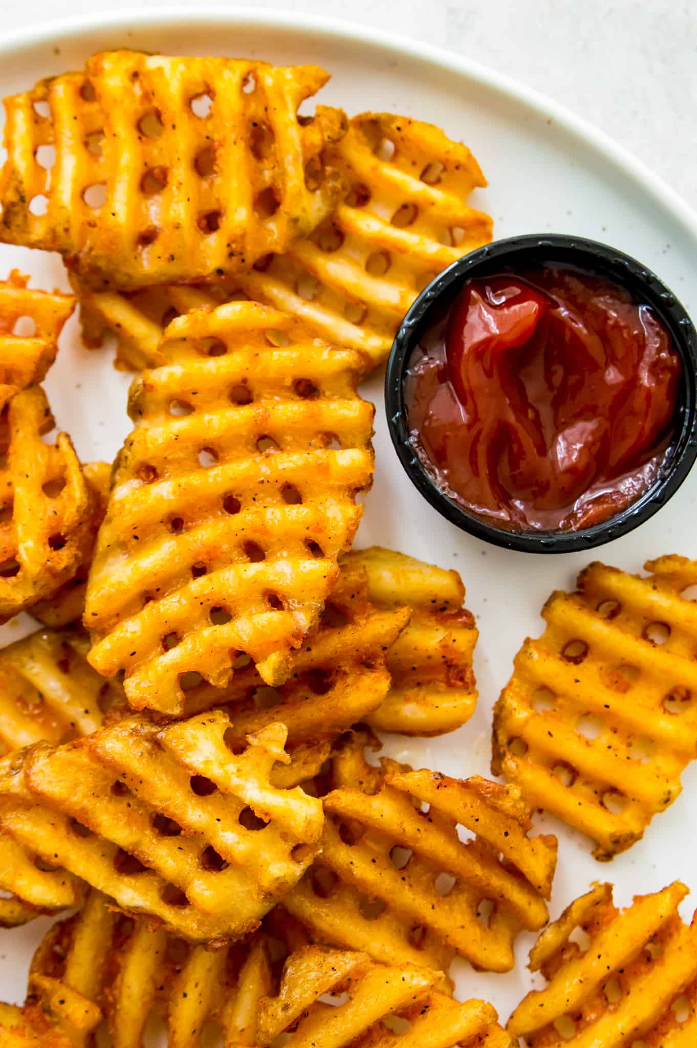 A plate of waffles fries with a side of ketchup.