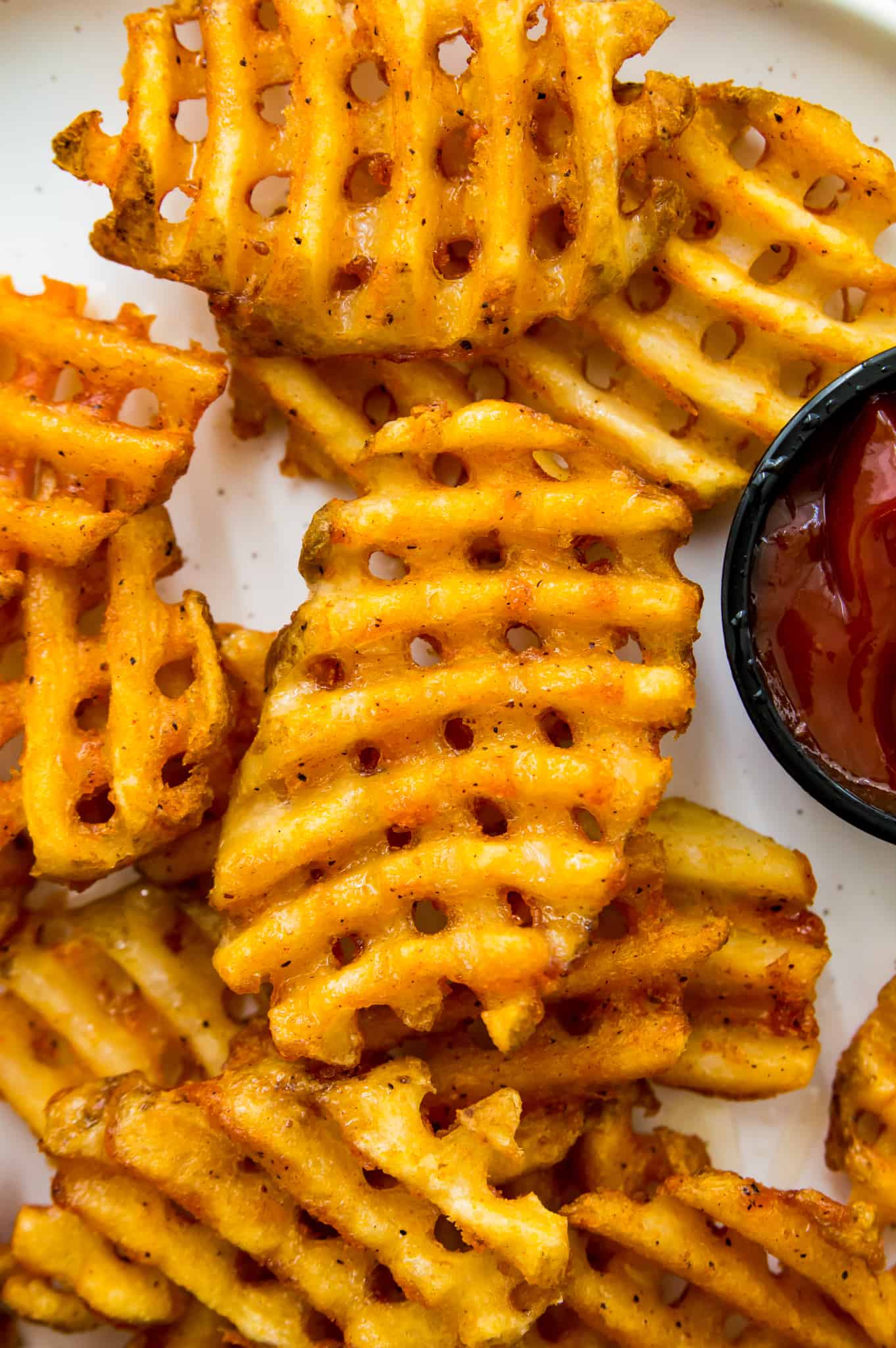 A plate of cooked waffle fries with ketchup beside the fries.