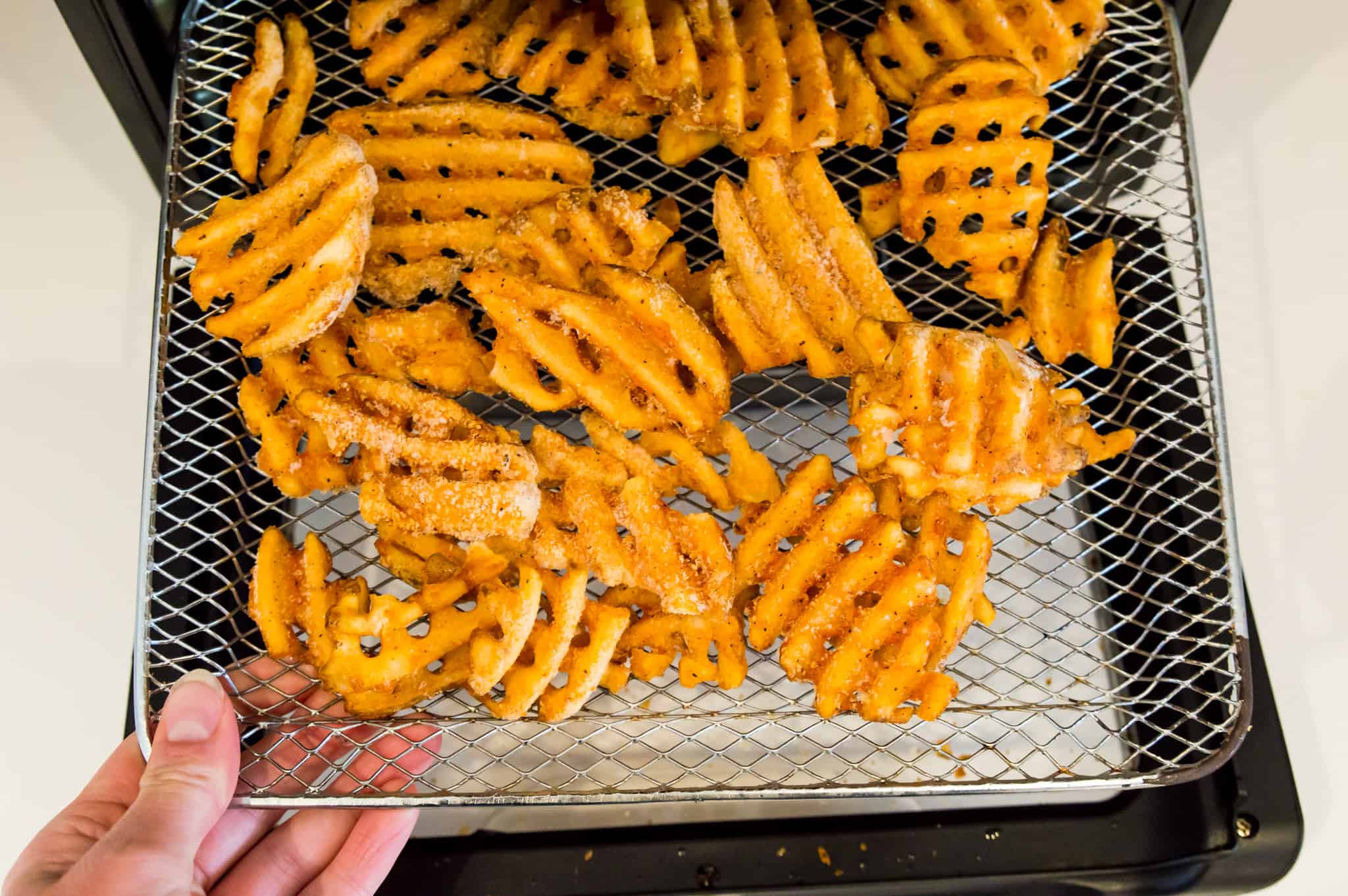 Frozen waffle fries on an air fryer tray.