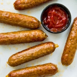 A plate of cooked bratwurst sausages with a dish of ketchup beside them.