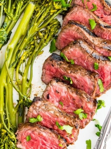 A plate of cooked steak with cooked broccoli beside it.