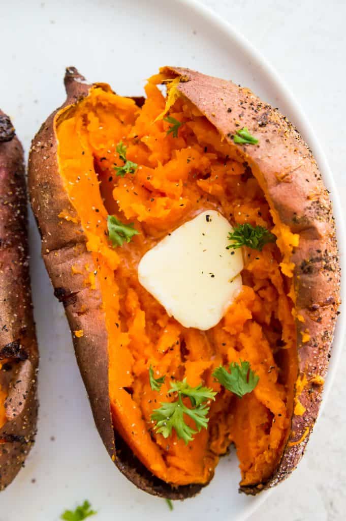 An air fryer baked sweet potato topped with butter and herbs on a plate
