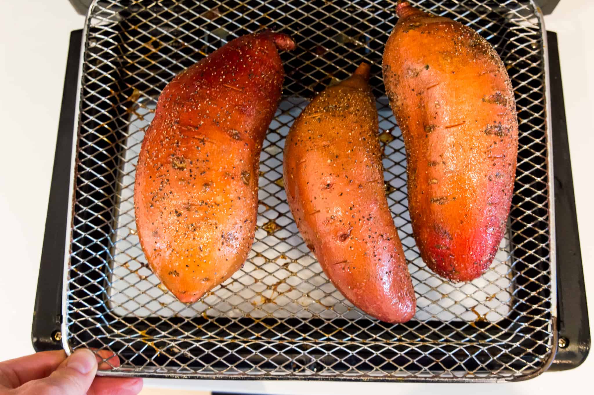 Three whole sweet potatoes on the rack of an air fryer oven.