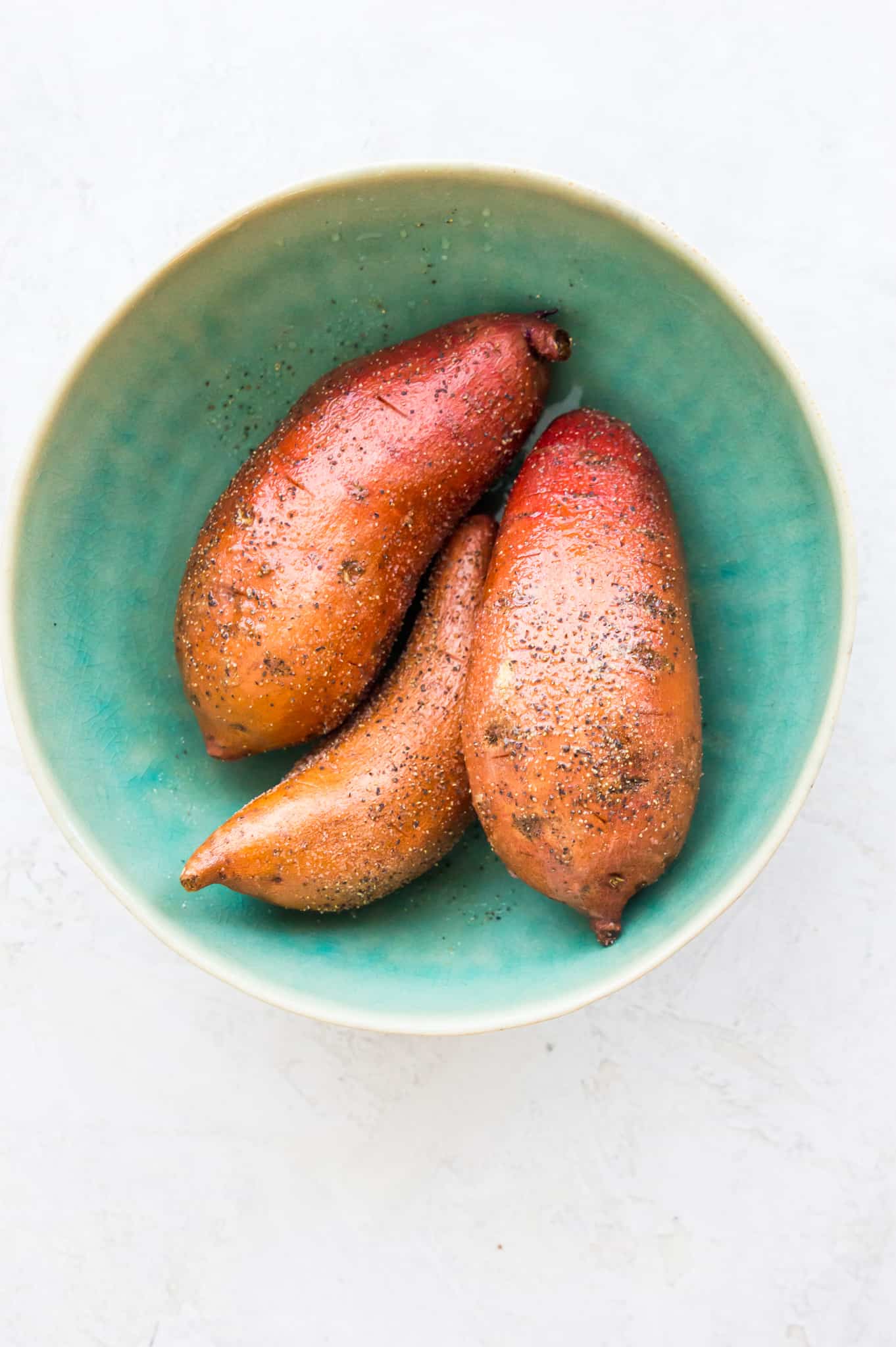 Three whole sweet potatoes in a bowl.