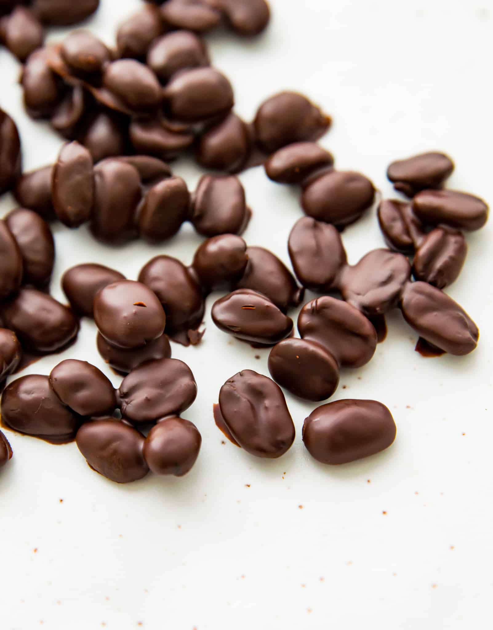 A bunch of chocolate covered espresso beans hardening on a white sheet of parchment paper
