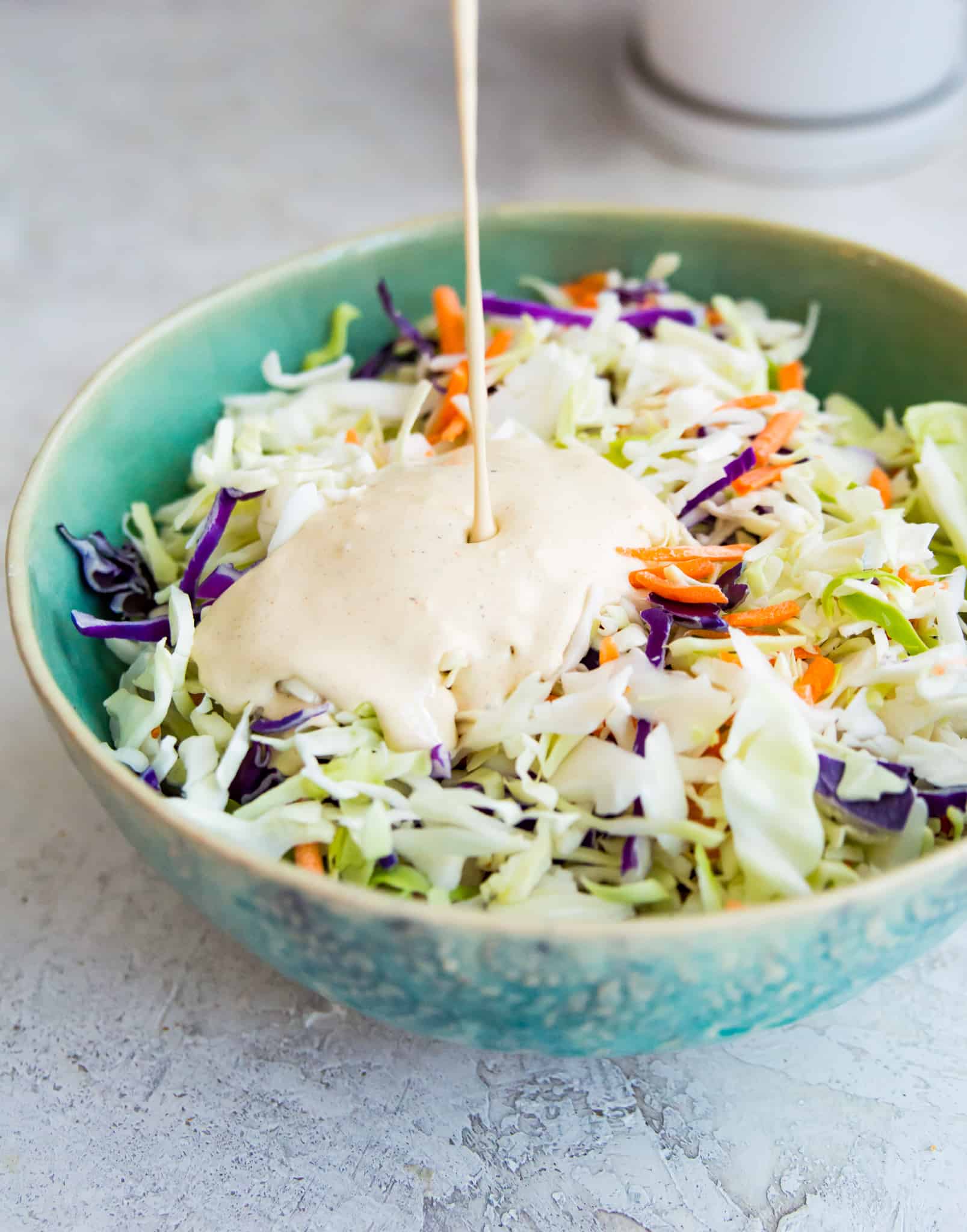 A creamy dressing being poured over a bowl of coleslaw.