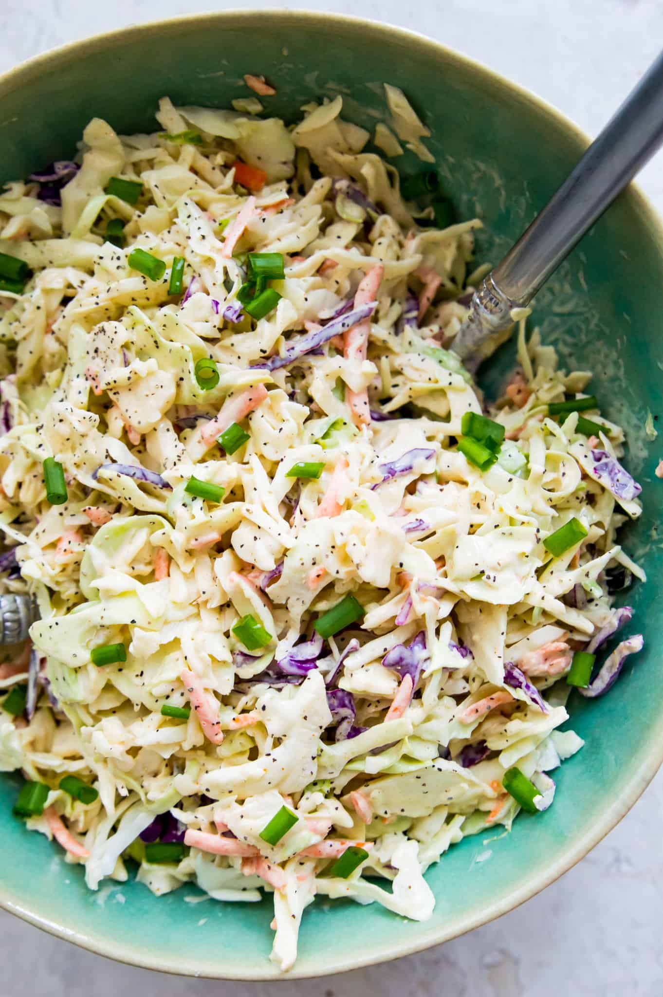 A bowl of coleslaw with a spoon in it.