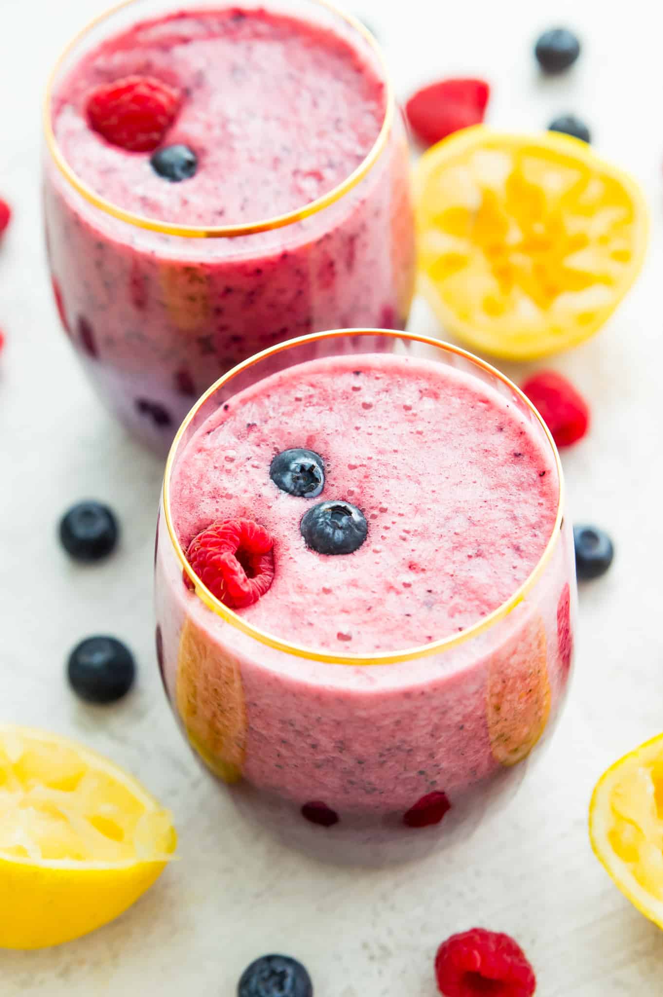 Two glasses of lemonade smoothie topped with blueberries and raspberries. 