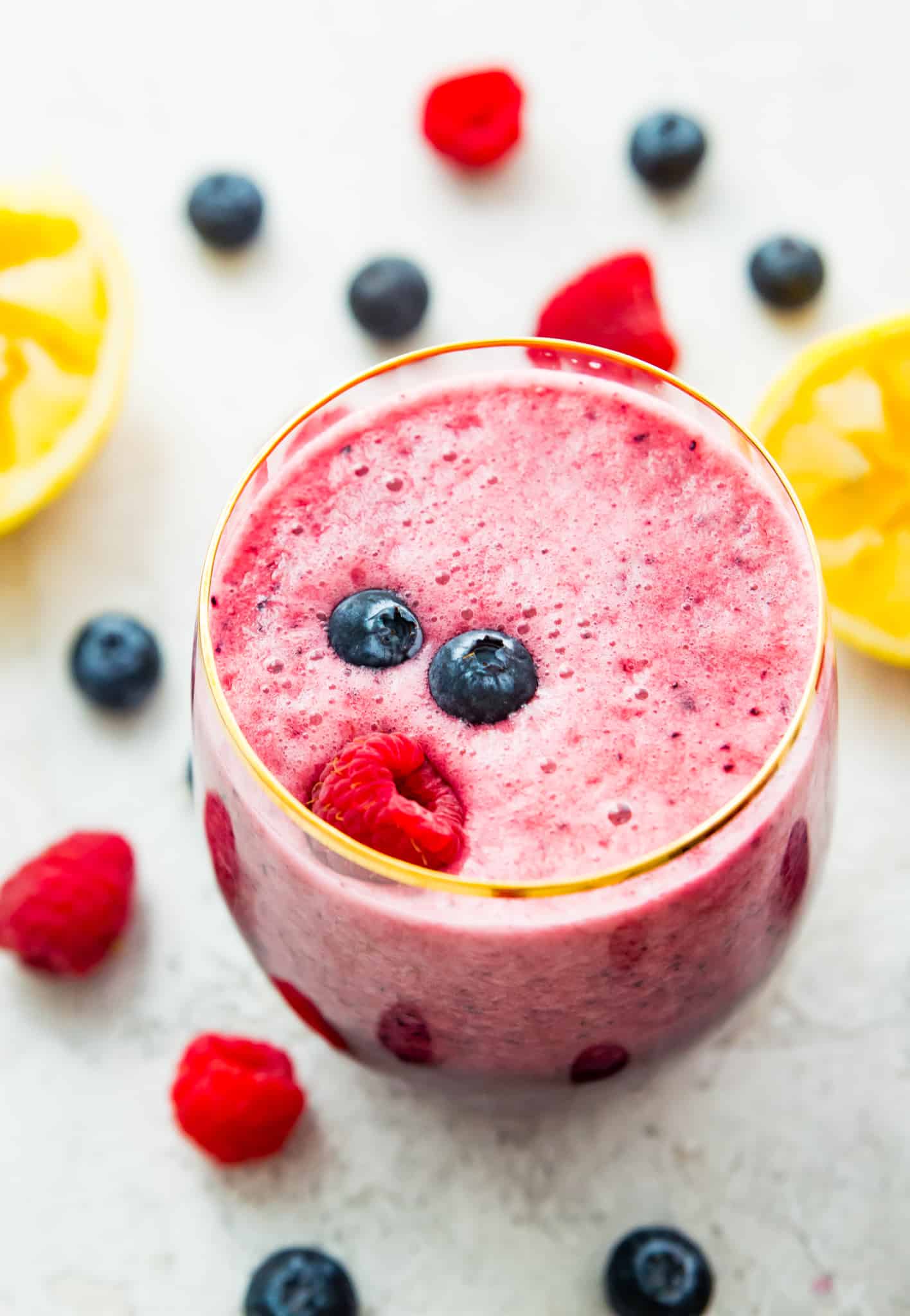 A berry lemonade smoothie in a glass with a raspberry and blueberries on top.