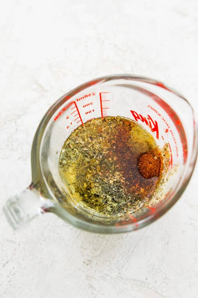 A glass measuring cup filled with the ingredients for making a Mexican chicken marinade. 