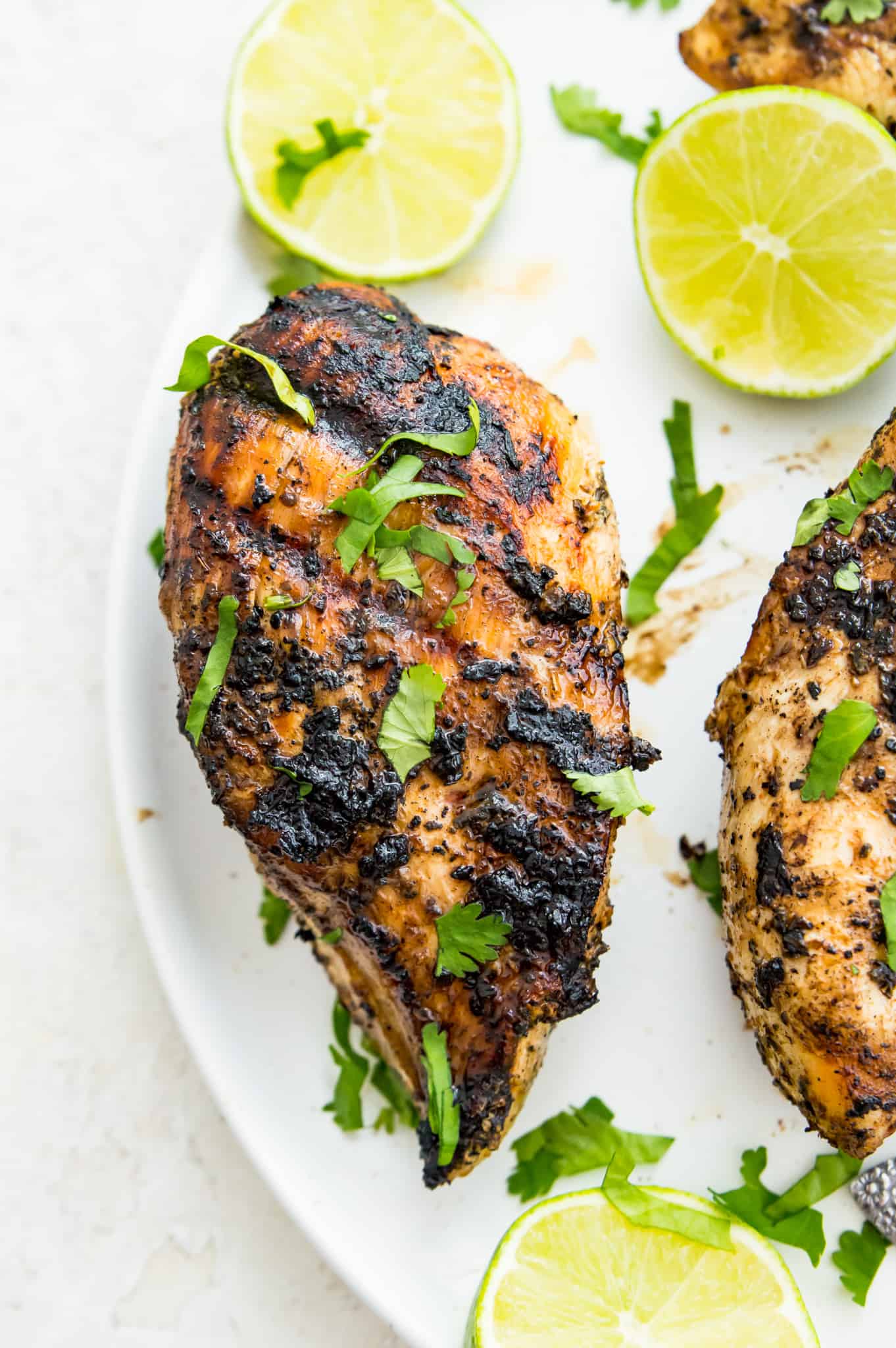 charred grilled Mexican chicken A piece of grilled Mexican chicken garnished with cilantro and surrounded by limes on a plate.