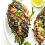 A piece of grilled chicken on a plate garnished with fresh cilantro.