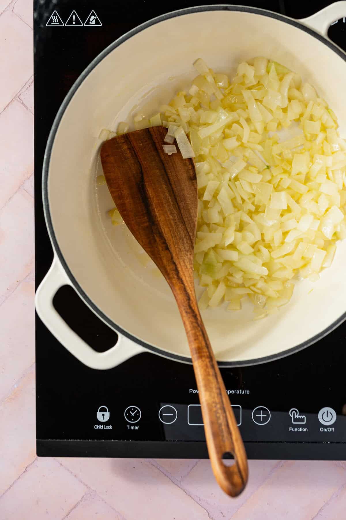 Chopped onion cooking in a pot with a wooden spoon in it.