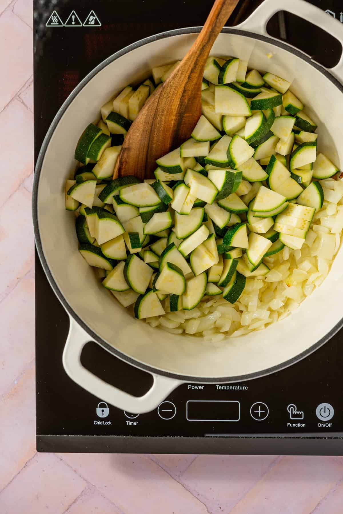 A pot with chopped zucchini and onion in it with a spoon stirring the vegetables.