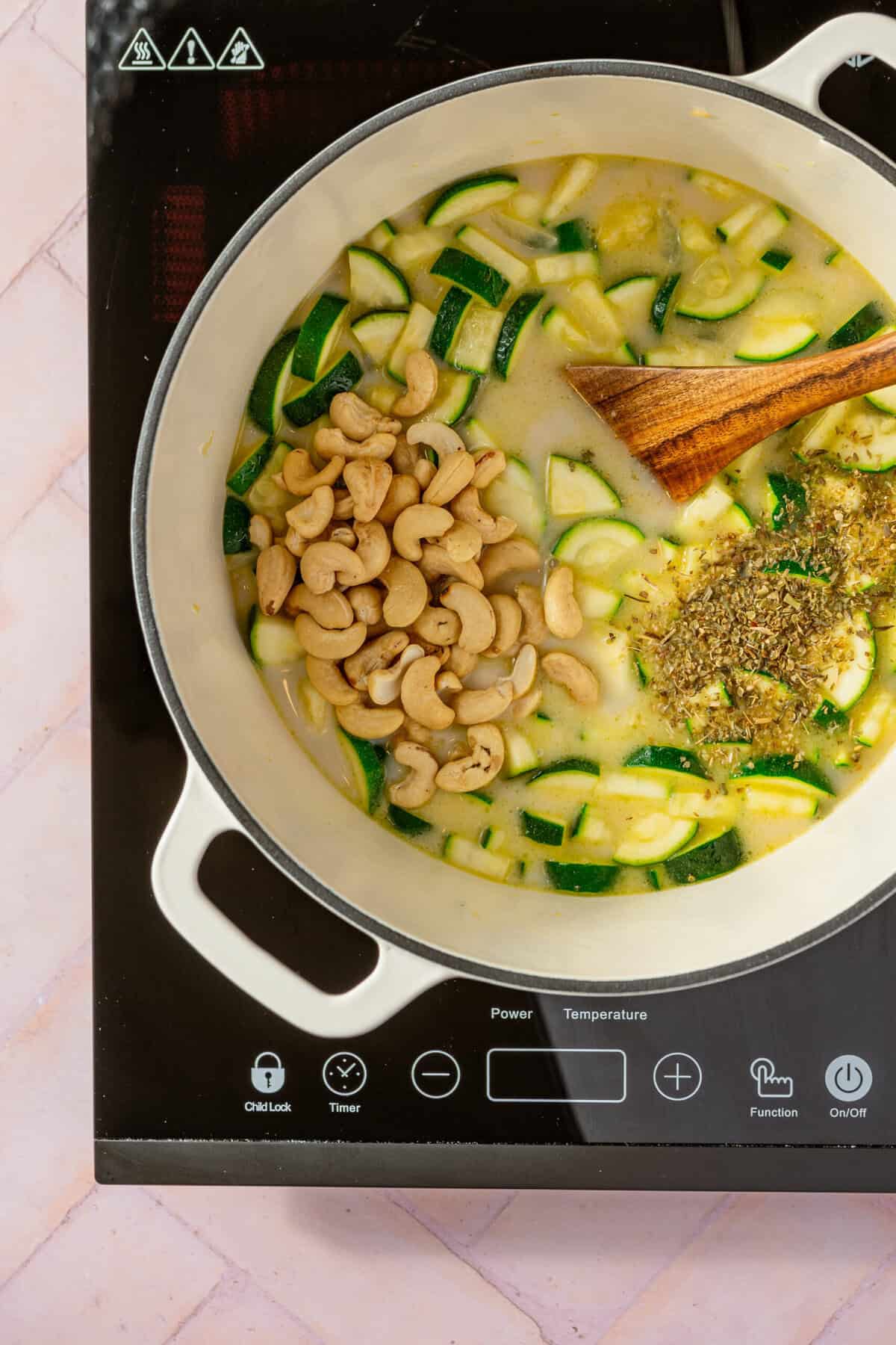 A pot with chopped zucchini, cashews, spices and coconut milk in it.
