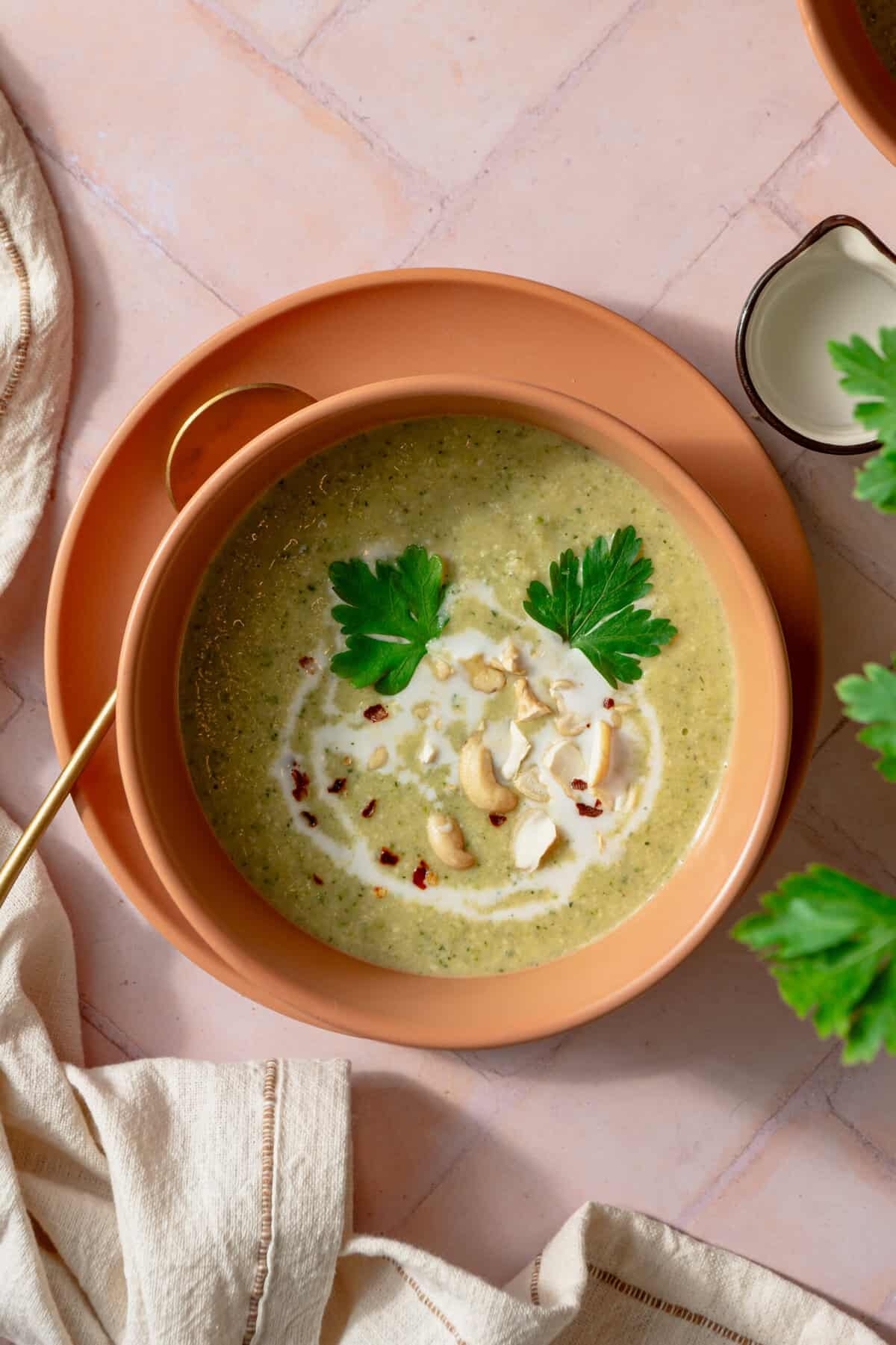 A bowl of creamy zucchini soup topped with chopped cilantro and raw cashew pieces.