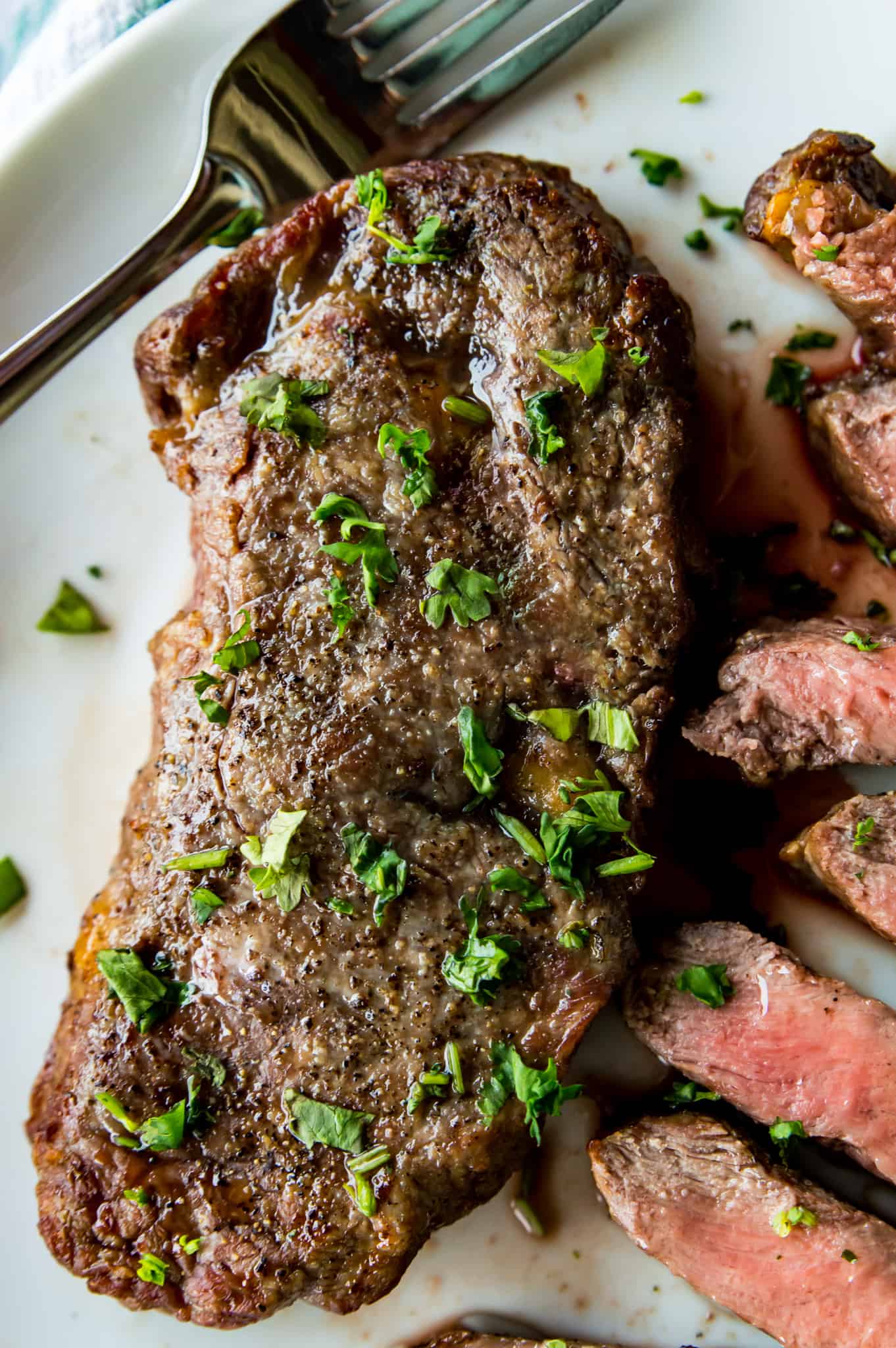 A piece of steak on a plate, seasoned with cilantro with a cut steak next to it. 