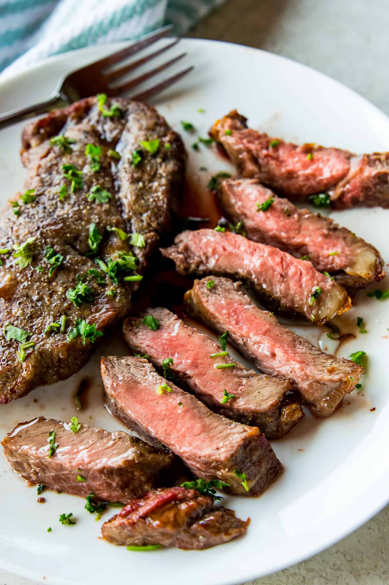 A piece of medium rare cut steak on a plate garnished with fresh chopped parsley.