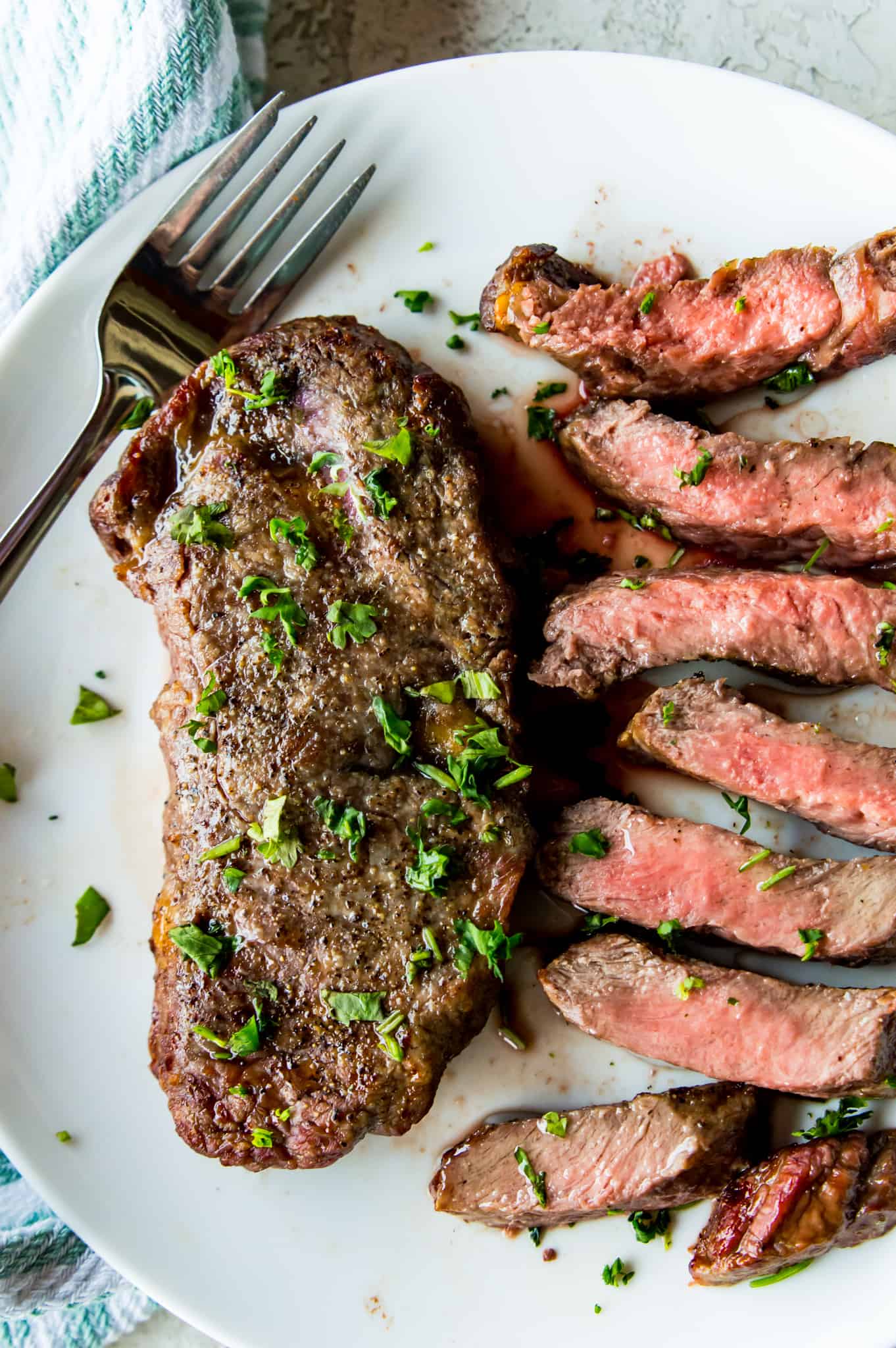 Two pieces of cooked steak on a plate, one that is cut up and one that is whole. 