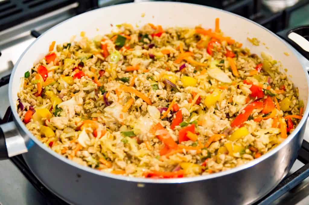 A pan on the stovetop filled with cooked ground pork, shredded cabbage and chopped bell peppers. 