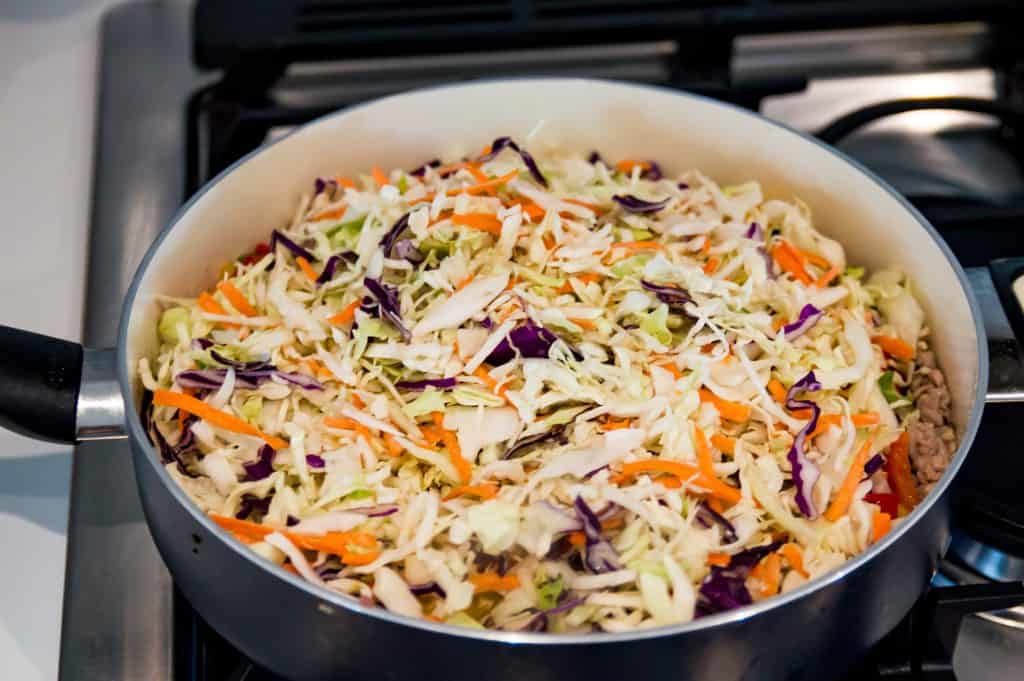 A pan on the stovetop filled with cooked ground pork and shredded cabbage. 
