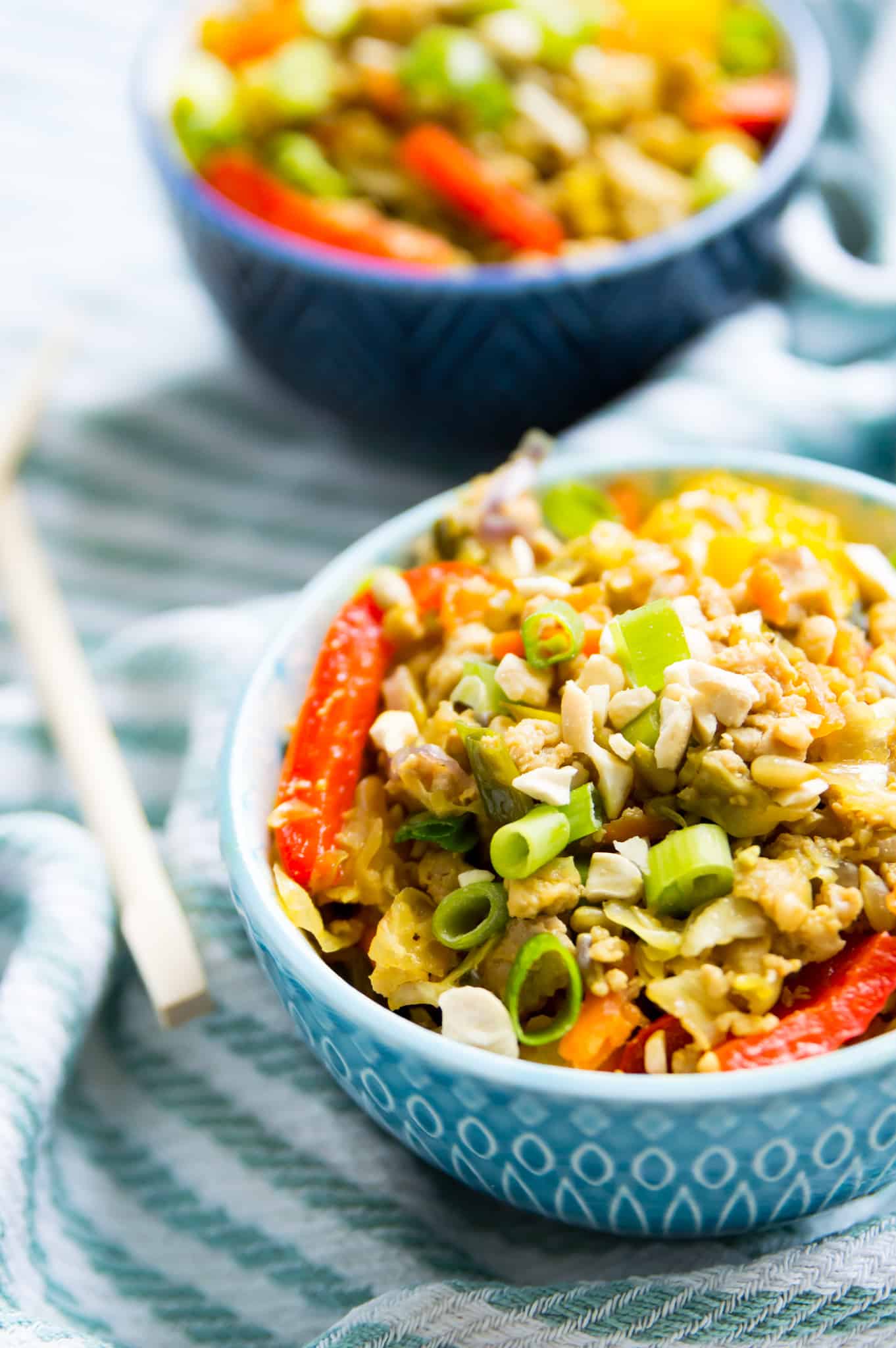 A bowl of egg roll in a bowl toped with chopped green onion and crushed peanuts with chop sticks next to the bowl.