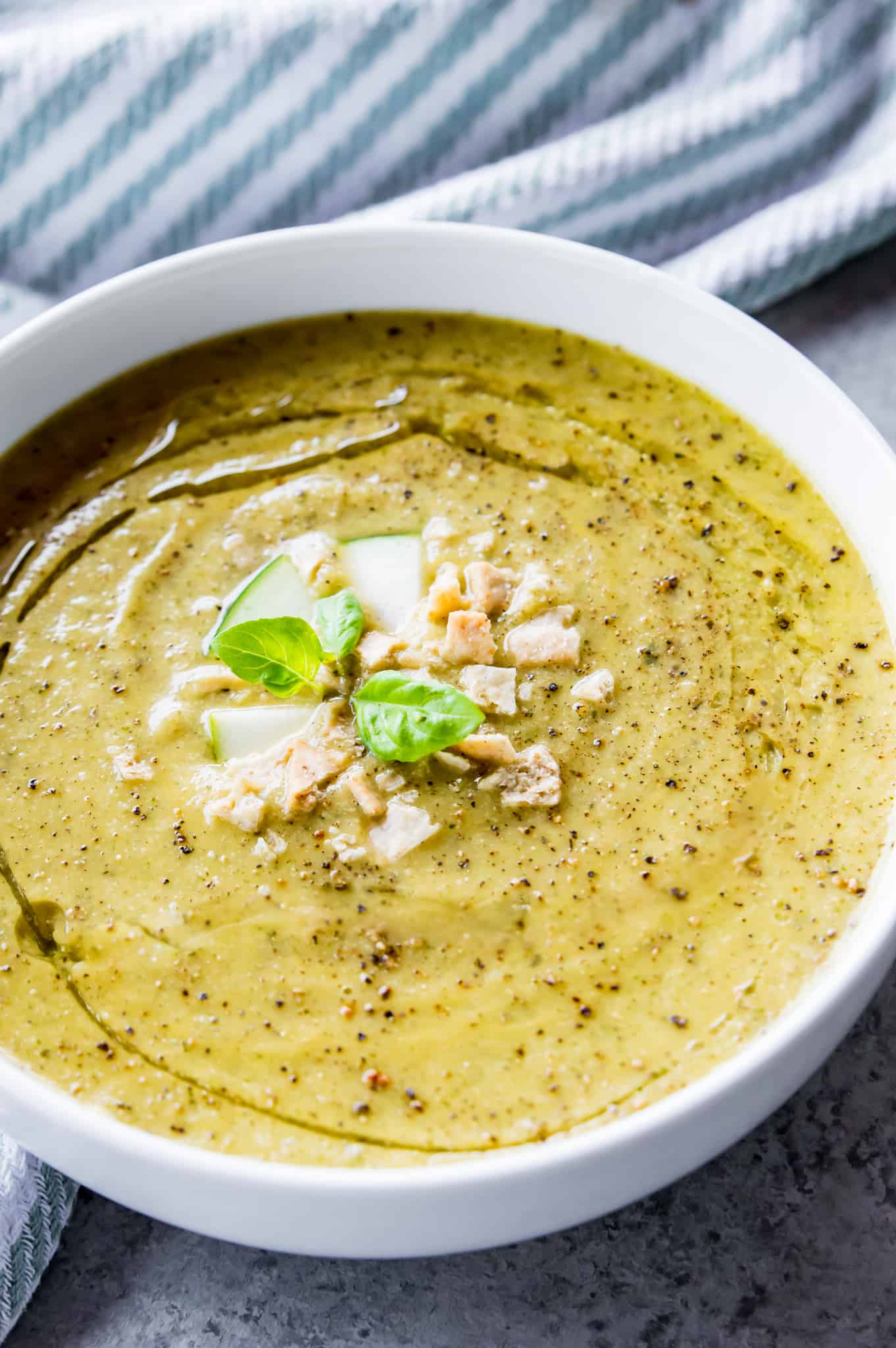 A bowl of vegan zucchini soup topped with crushed crackers and fresh basil.