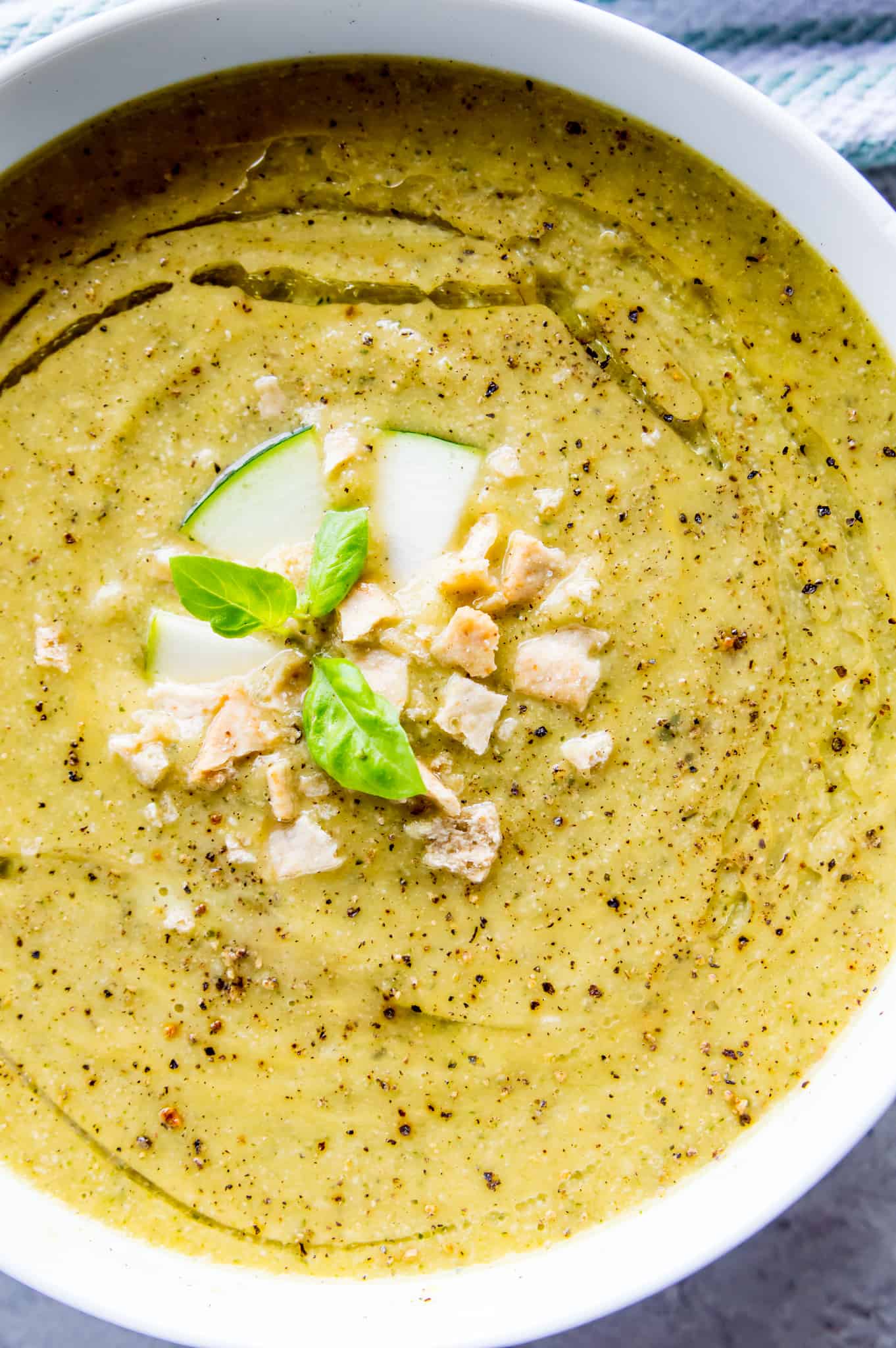 A bowl of creamy vegan zucchini soup topped with crackers, fresh basil and black pepper.