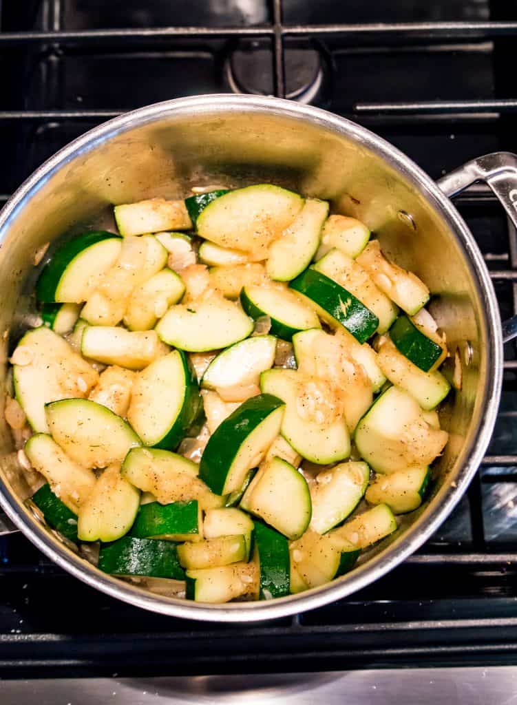 A large pot on the stove with onion and chopped zucchini cooking in it.
