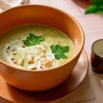 A bowl of creamy zucchini soup topped with fresh cilantro and raw cashews.
