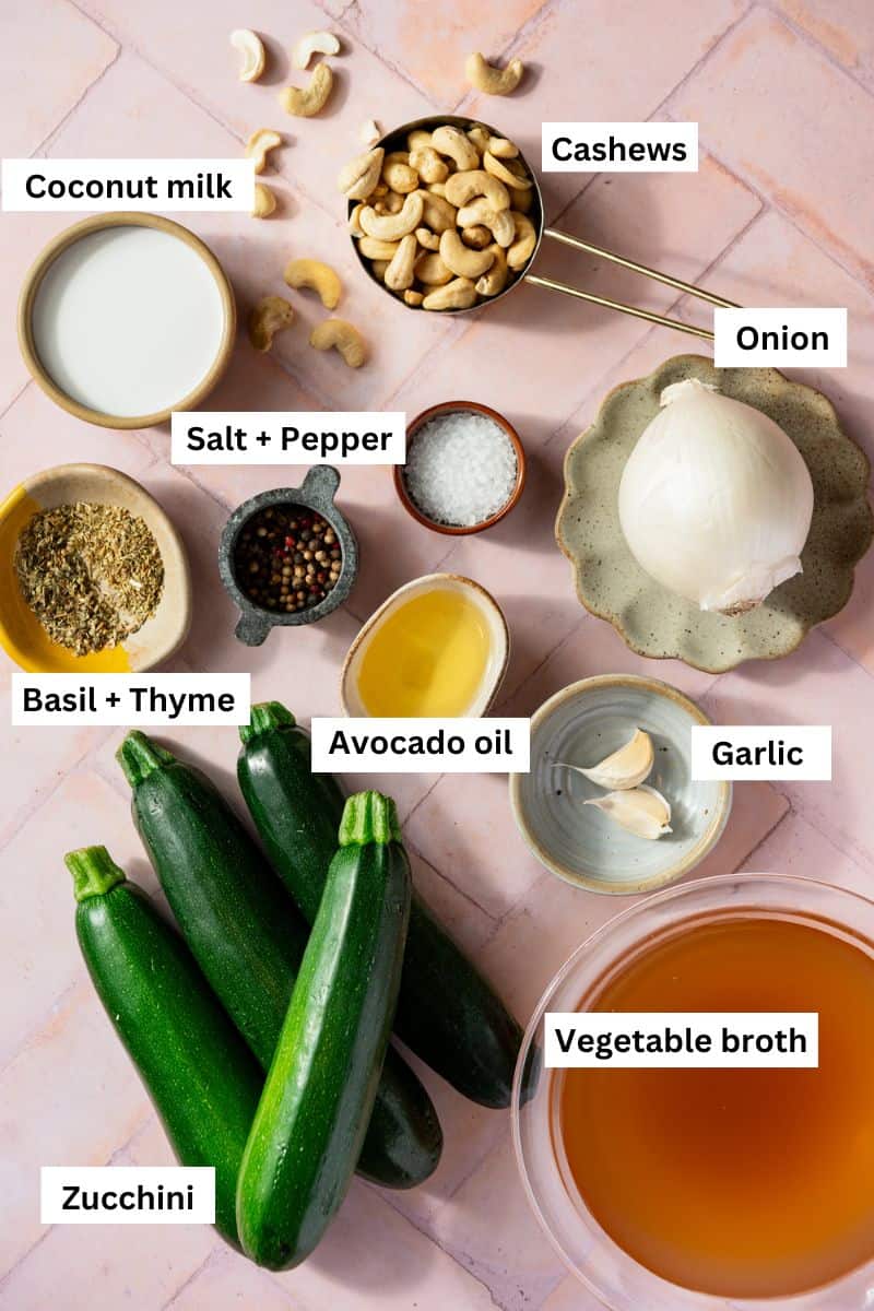 The ingredients needed to make a vegan zucchini soup separated into bowls including zucchini, cashews, broth, spices, garlic and onion.