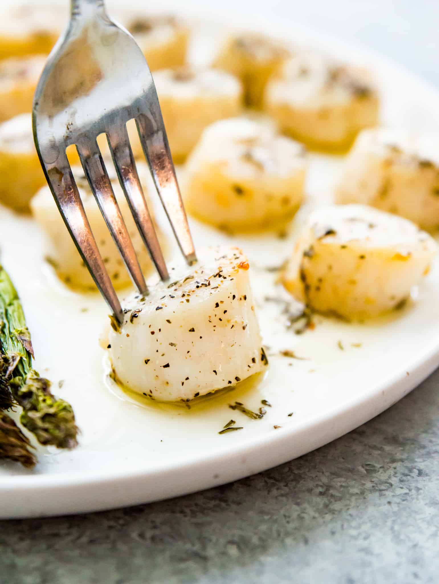 A plate of cooked scallops with lemon butter sauce on them and a fork piercing one of them. 