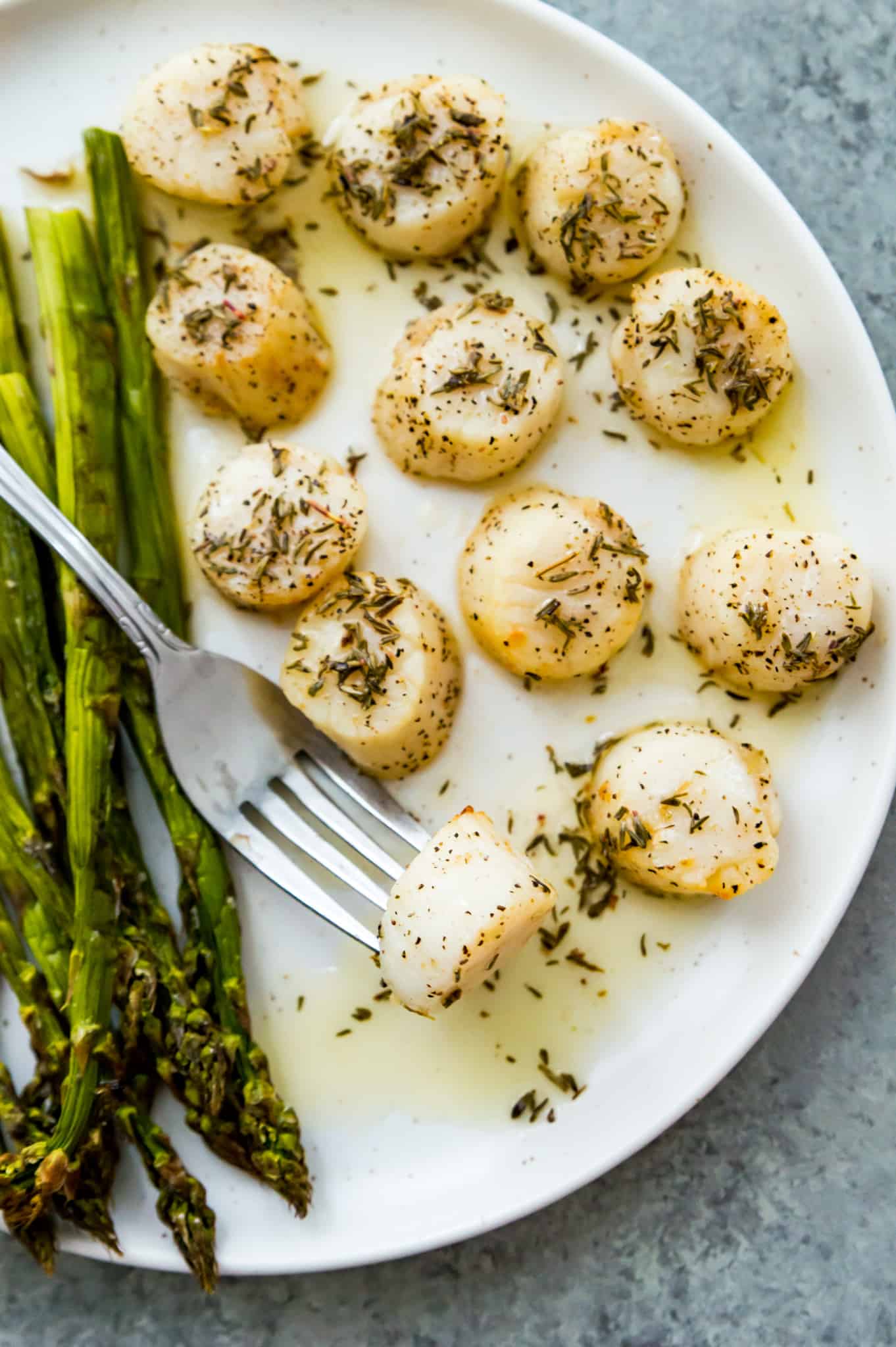 Scallops on a plate with cooked asparagus next to them.