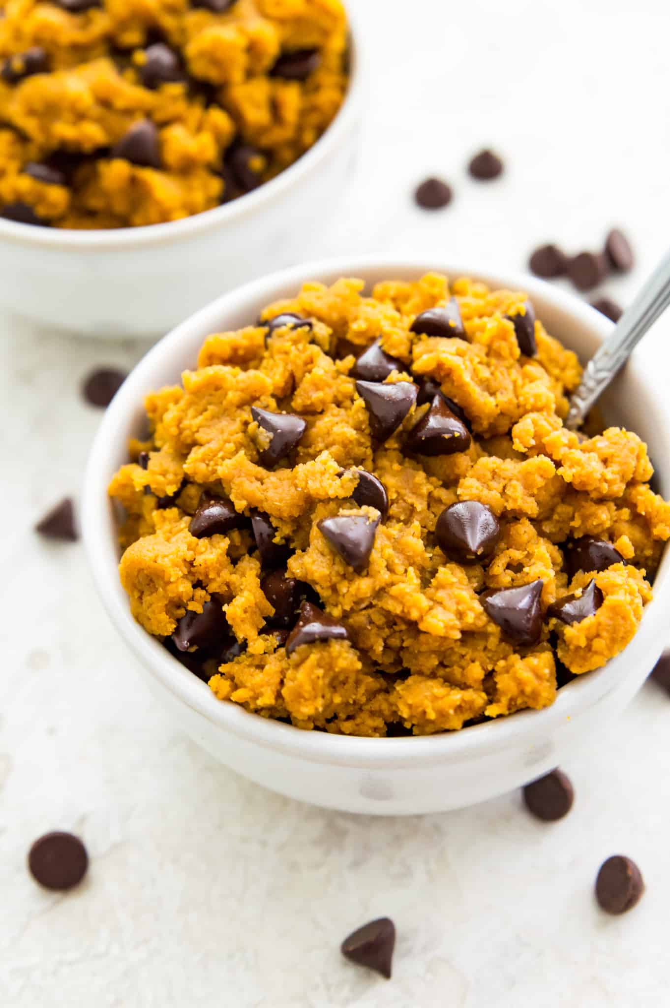 A bowl of edible pumpkin cookie dough with chocolate chips and a spoon in it.