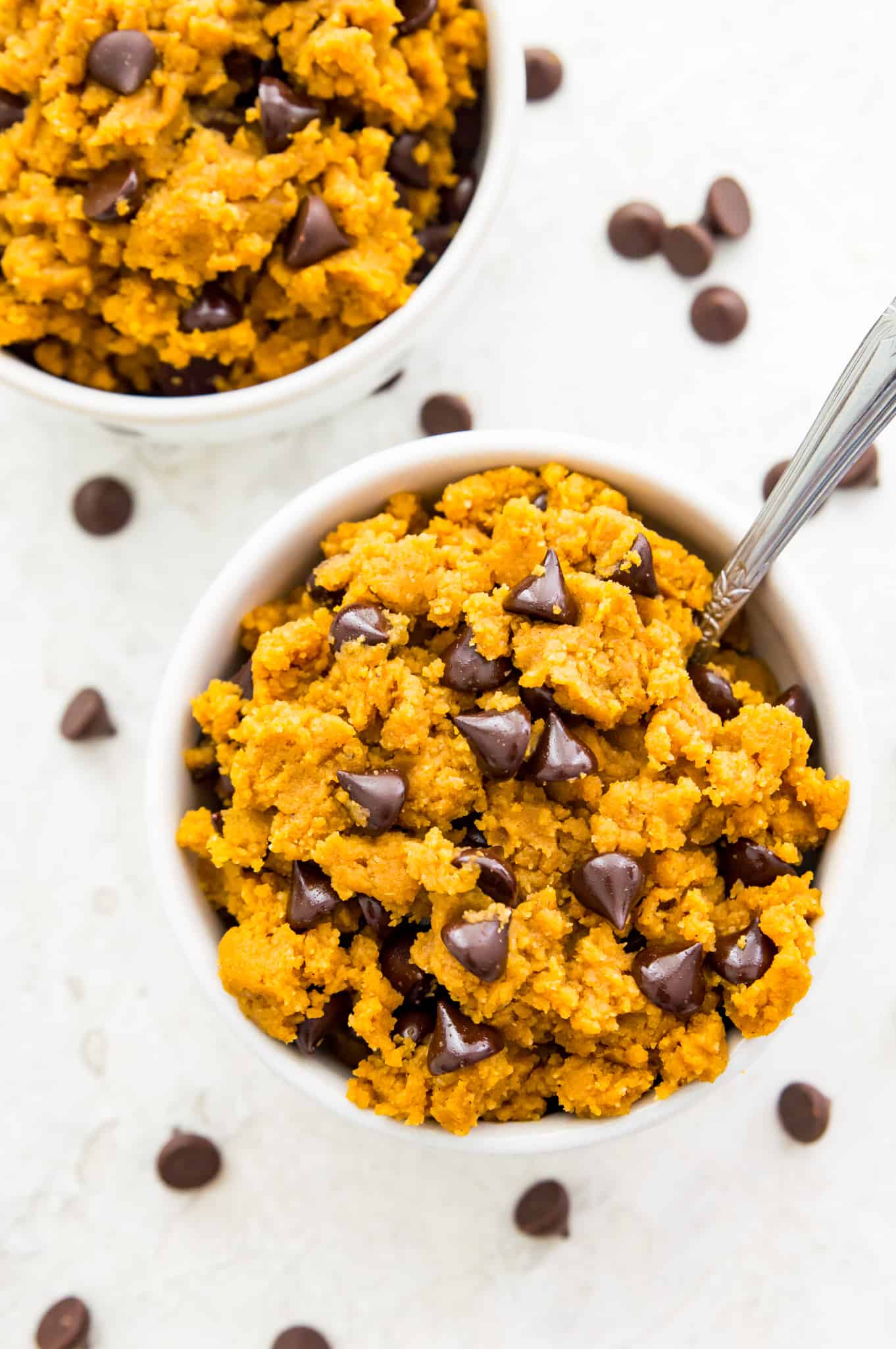 A bowl of edible pumpkin chocolate chip cookie dough with a spoon in it.