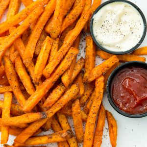 Cooked sweet potato fries on a plate with sides of ketchup and mayonnaise.