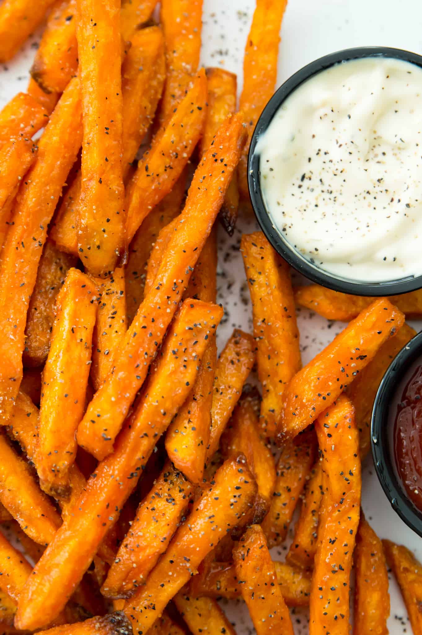A plate of sweet potato fries cooked in an air fryer with a side of ketchup and aioli
