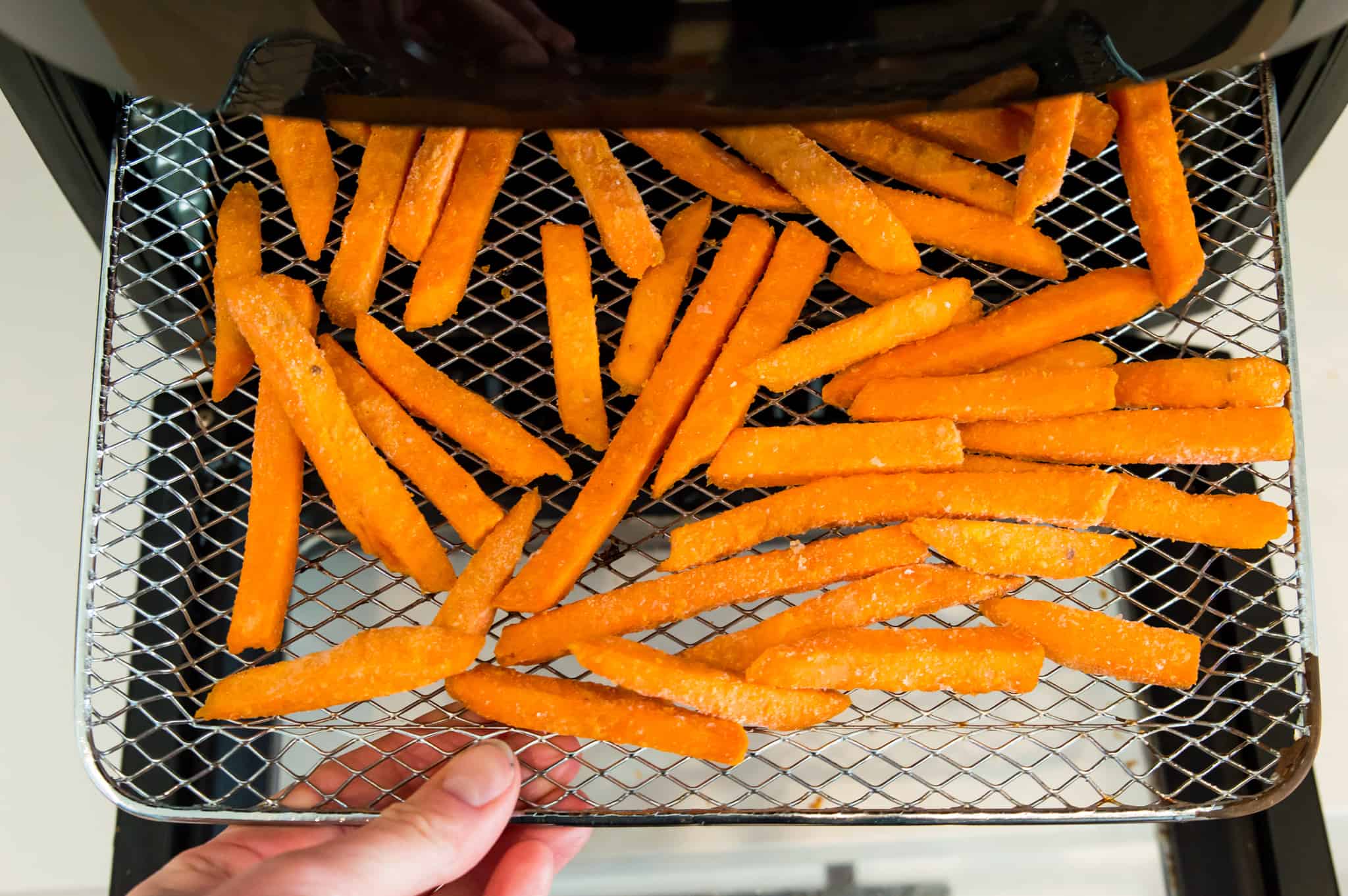 Frozen sweet potato fries on the tray of an air fryer.