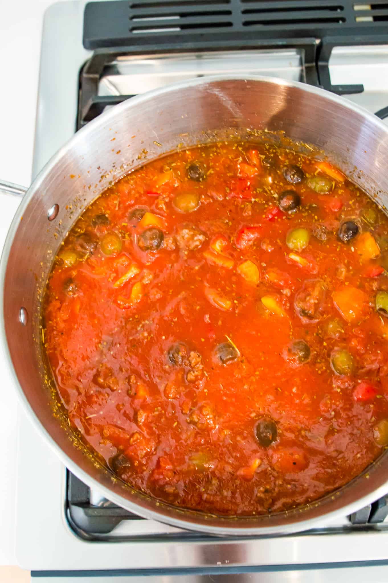 A pot filled with a tomato sauce with olives and ground beef in it.